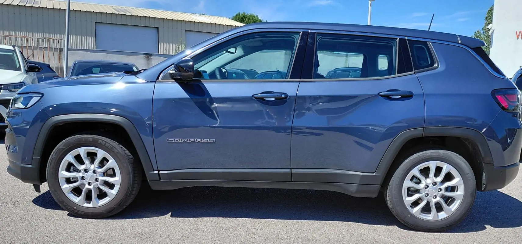 Vue de profil côté gauche d'un Jeep Compass bleu 2025 avec jantes alliage 18 pouces et logo visible sur la porte.
