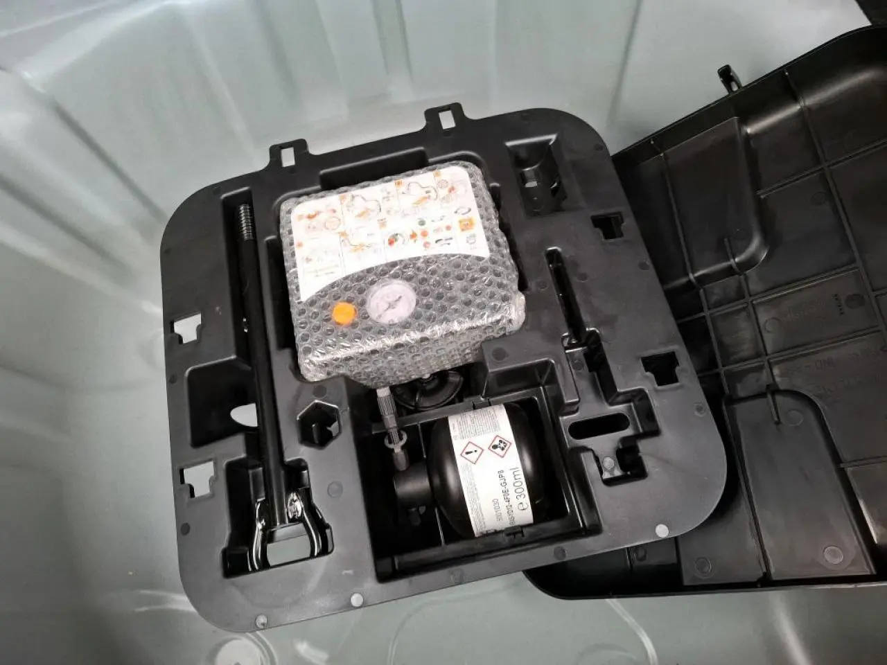 Détail du kit de gonflage pneumatiques dans le coffre d'une Renault Clio blanche 2024, version Tce 90 cv.