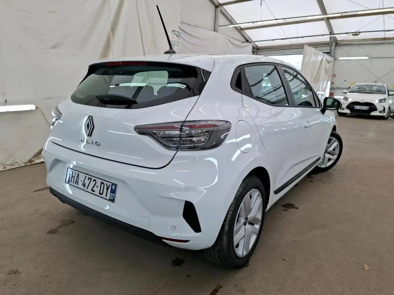 Vue 3/4 arrière droite d'une Renault Clio blanche 2024 avec feux arrière LED et jantes 16 pouces en intérieur.