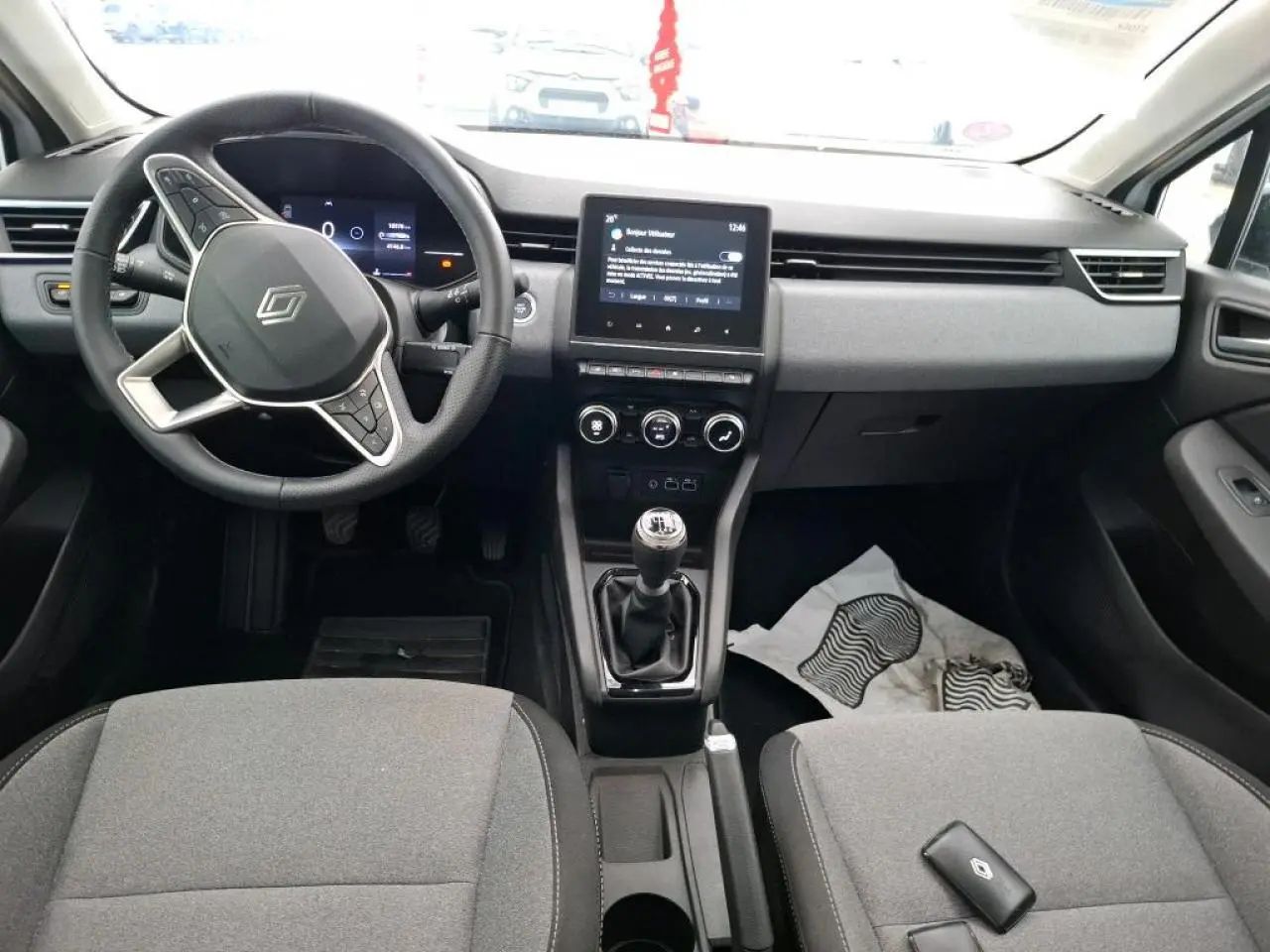 Vue intérieure avant de la Renault Clio blanche 2024, avec tableau de bord moderne et boîte manuelle.