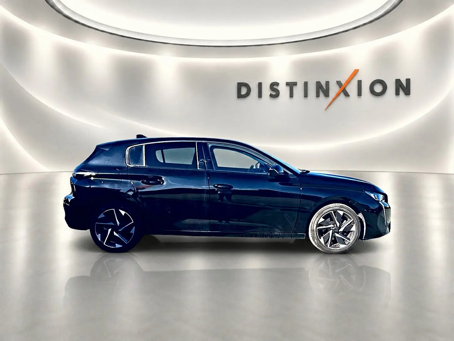 Profil droit d'une Peugeot 308 noire 2025 avec jantes alu stylisées, dans un showroom lumineux au mur blanc.