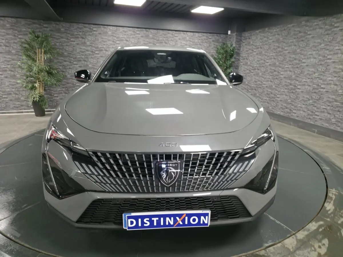 Vue frontale d'une Peugeot 408 gris métallisé avec calandre verticale et logo lion central, en showroom.