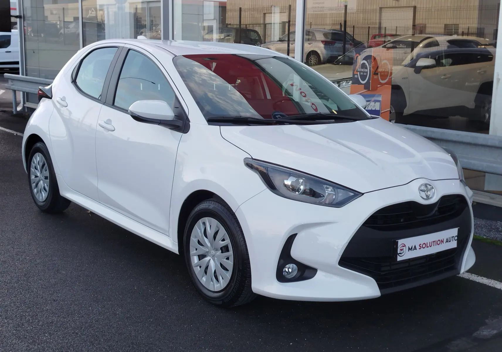 Toyota Yaris blanc pur vue 3/4 avant droit, avec calandre noire et jantes acier à enjoliveurs.