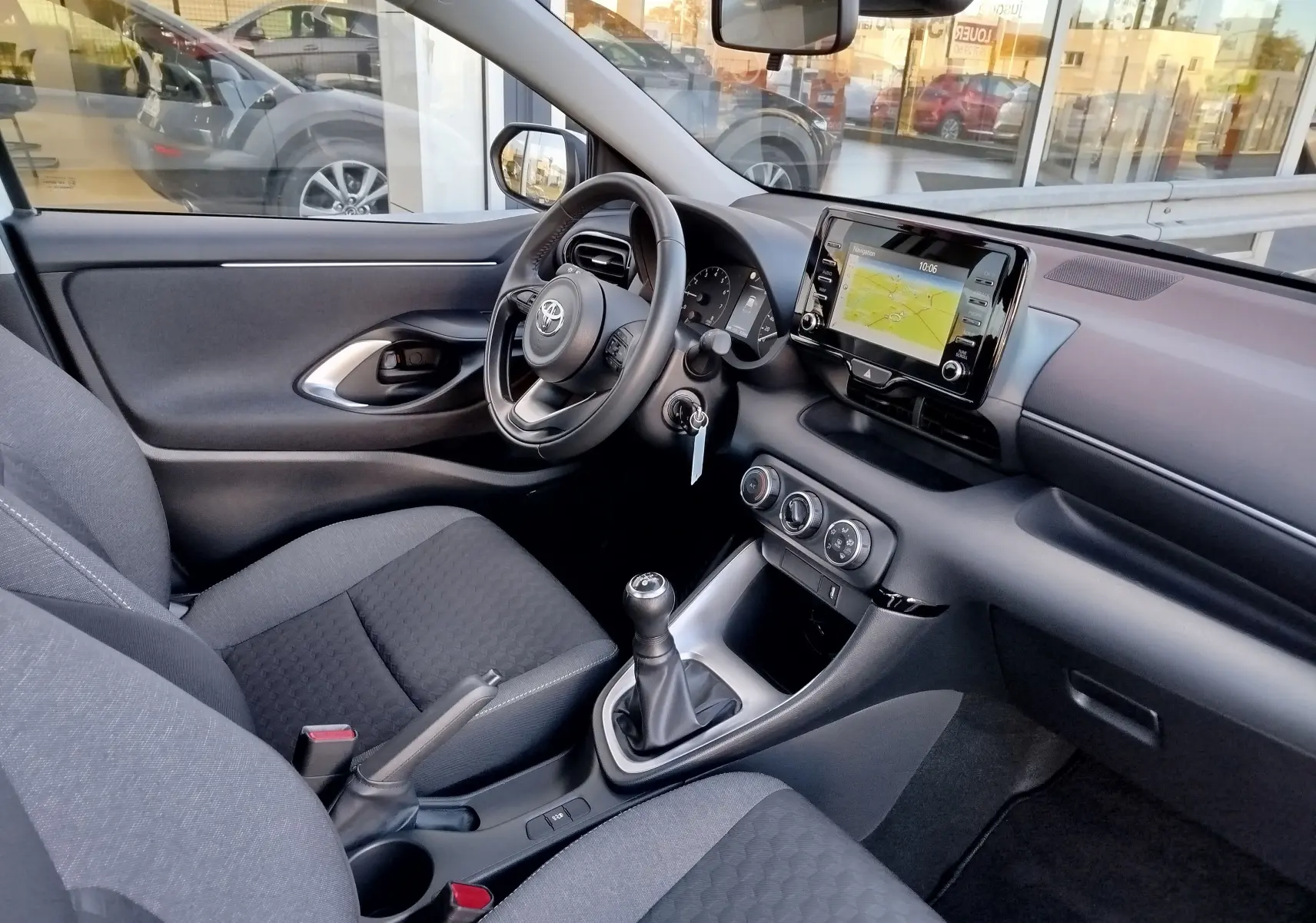 Vue intérieure côté conducteur de la Toyota Yaris blanche, mettant en valeur le tableau de bord et la boîte manuelle.