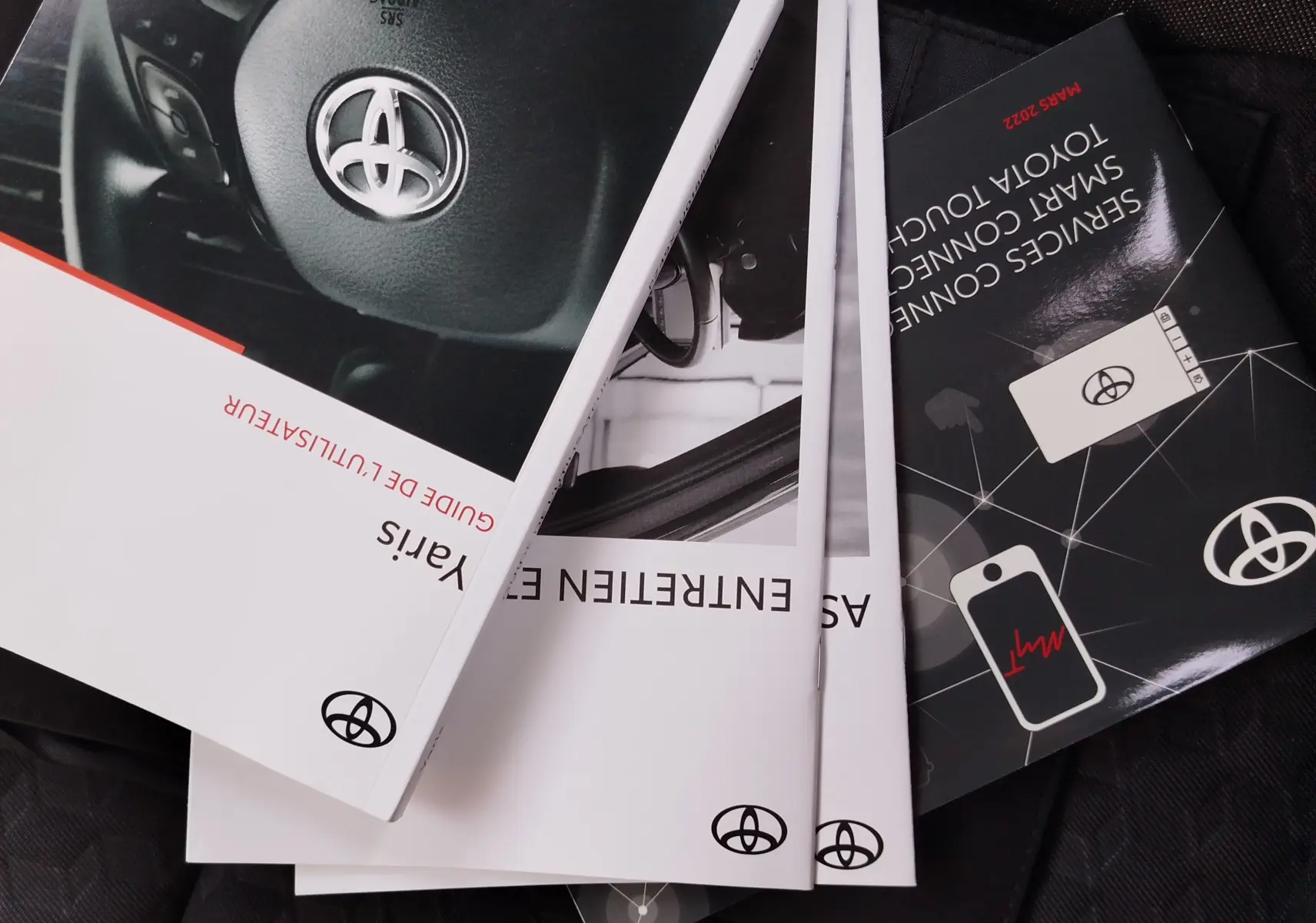 Image montrant plusieurs manuels d'utilisation Toyota Yaris 2023, posés en éventail sur un siège, avec logo Toyota visible.