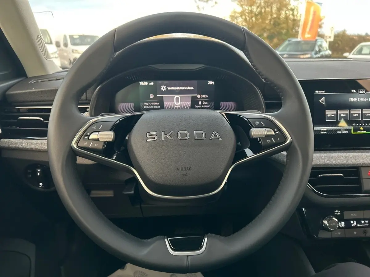 Vue rapprochée du volant cuir noir marqué SKODA et du tableau de bord numérique du SUV KAMIQ gris clair 2025.