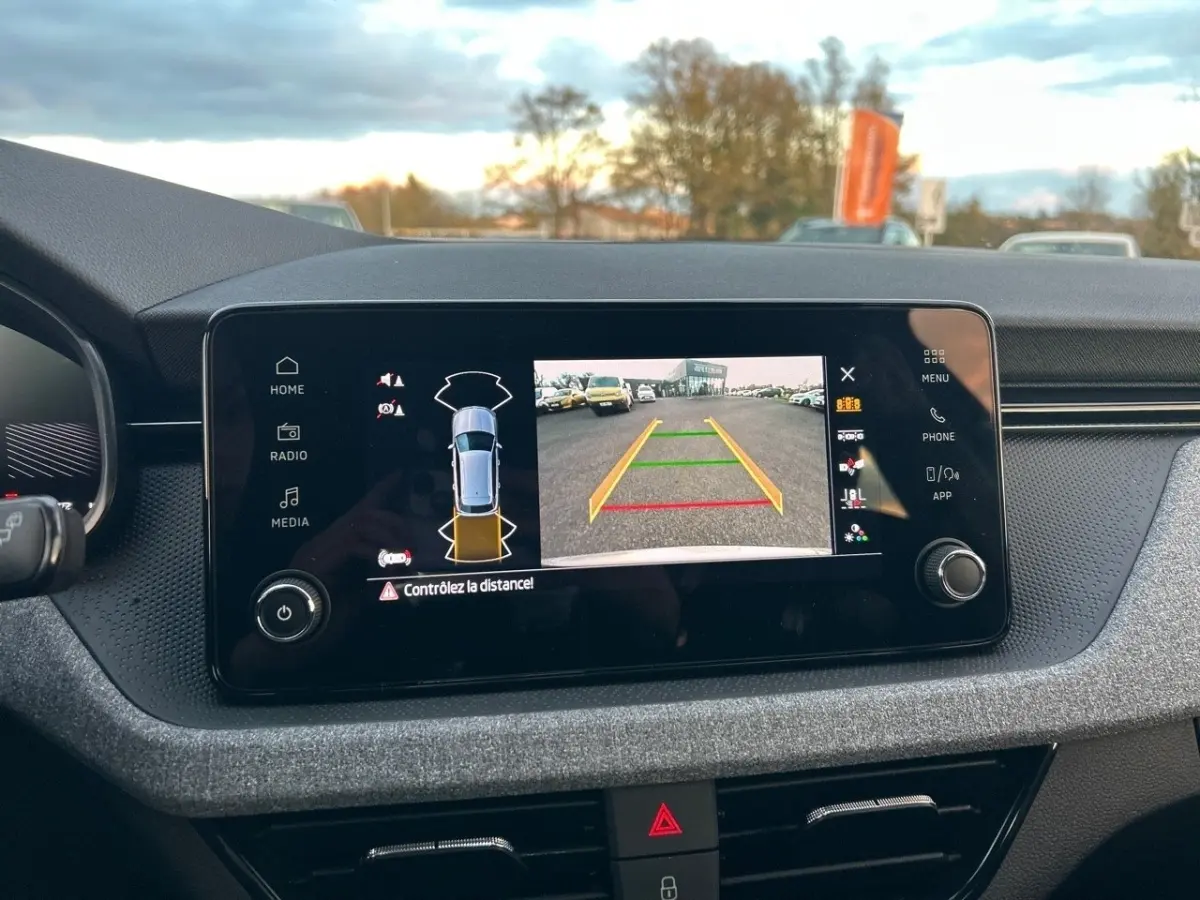 Écran tactile central du tableau de bord du Skoda Kamiq gris clair, affichant la caméra de recul et les capteurs de stationnement.