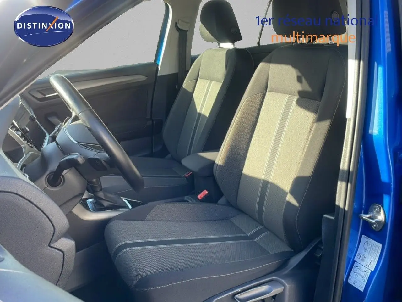 Vue intérieure côté conducteur du Volkswagen T-Roc bleu Ravenna, mettant en valeur les sièges en tissu gris avec surpiqûres.