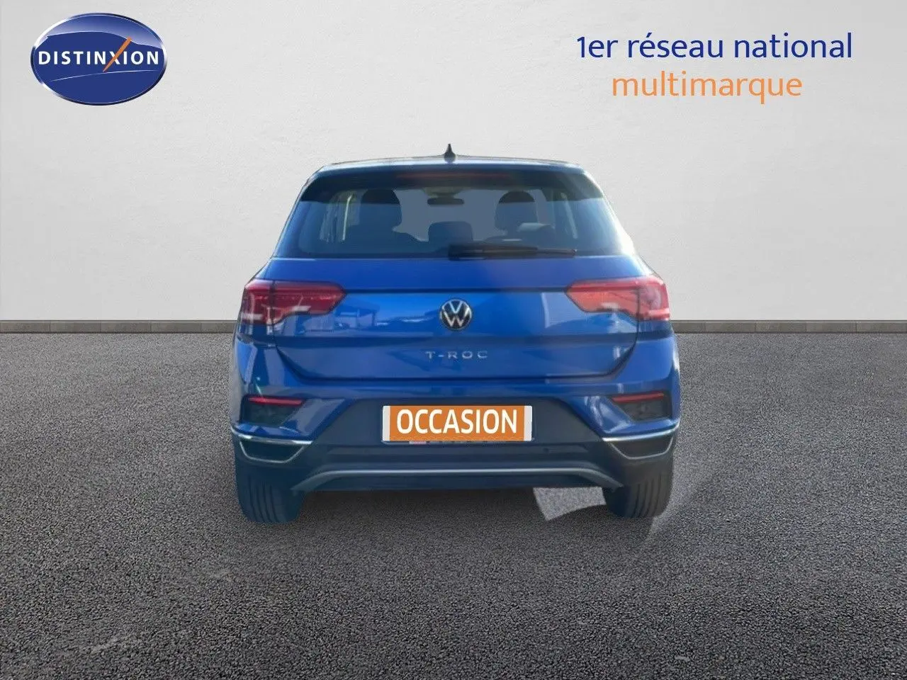 Vue arrière d'un Volkswagen T-Roc bleu Ravenna métallisé avec plaque occasion sur un sol goudronné.