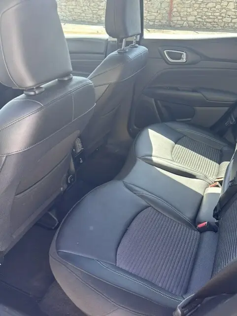 Vue intérieure arrière droite du Jeep Compass 2025 noir, montrant les sièges en cuir et tissu avec accoudoir central.