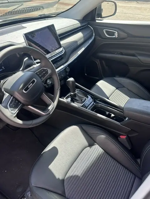 Vue intérieure côté conducteur du Jeep Compass 2025 noir, avec écran tactile, volant multifonction et accoudoir central.