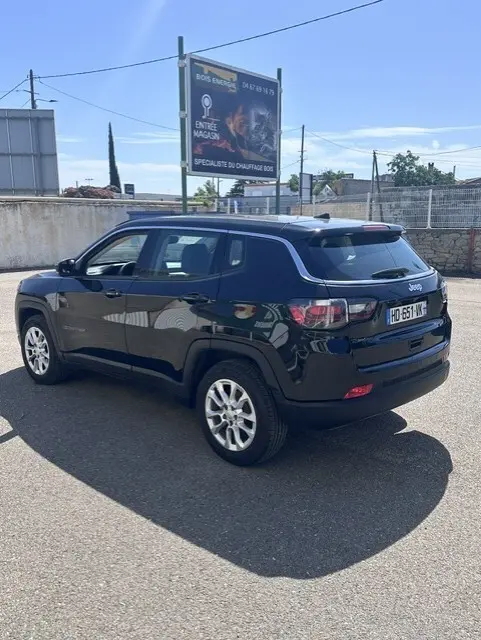Jeep Compass noir vue 3/4 arrière droit, jantes alliage 18 pouces, toit noir avec barres de toit, stationné en extérieur.