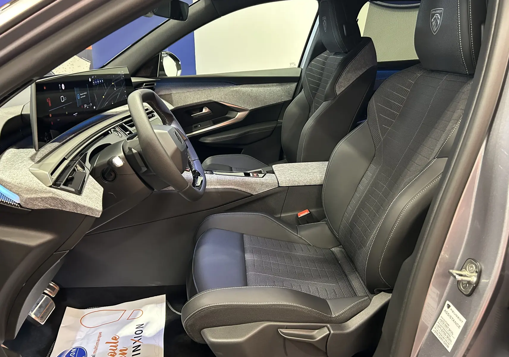 Vue intérieure côté conducteur du Peugeot 5008 III GT Hybrid 145 avec sièges noirs et tableau de bord moderne gris Artense.