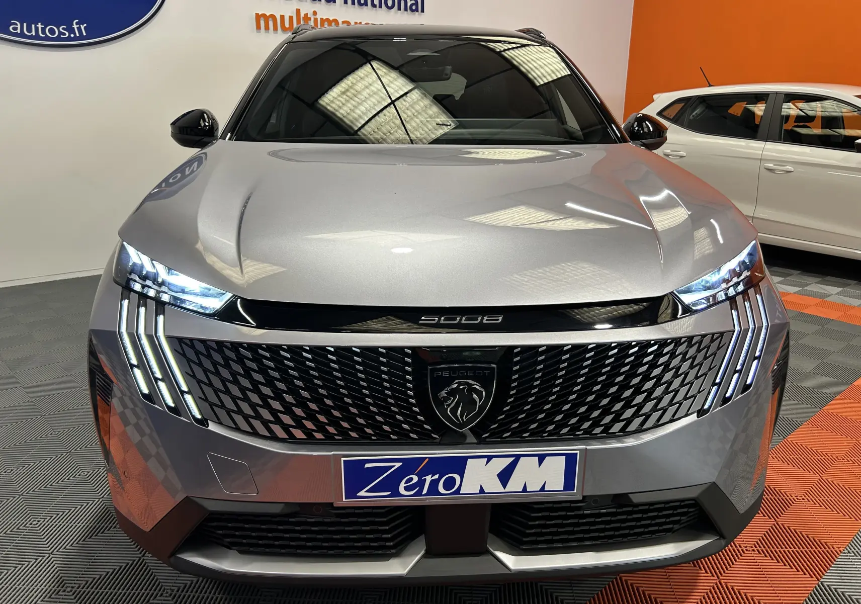 Vue frontale du Peugeot 5008 gris Artense avec phares LED allumés et calandre noire distinctive.