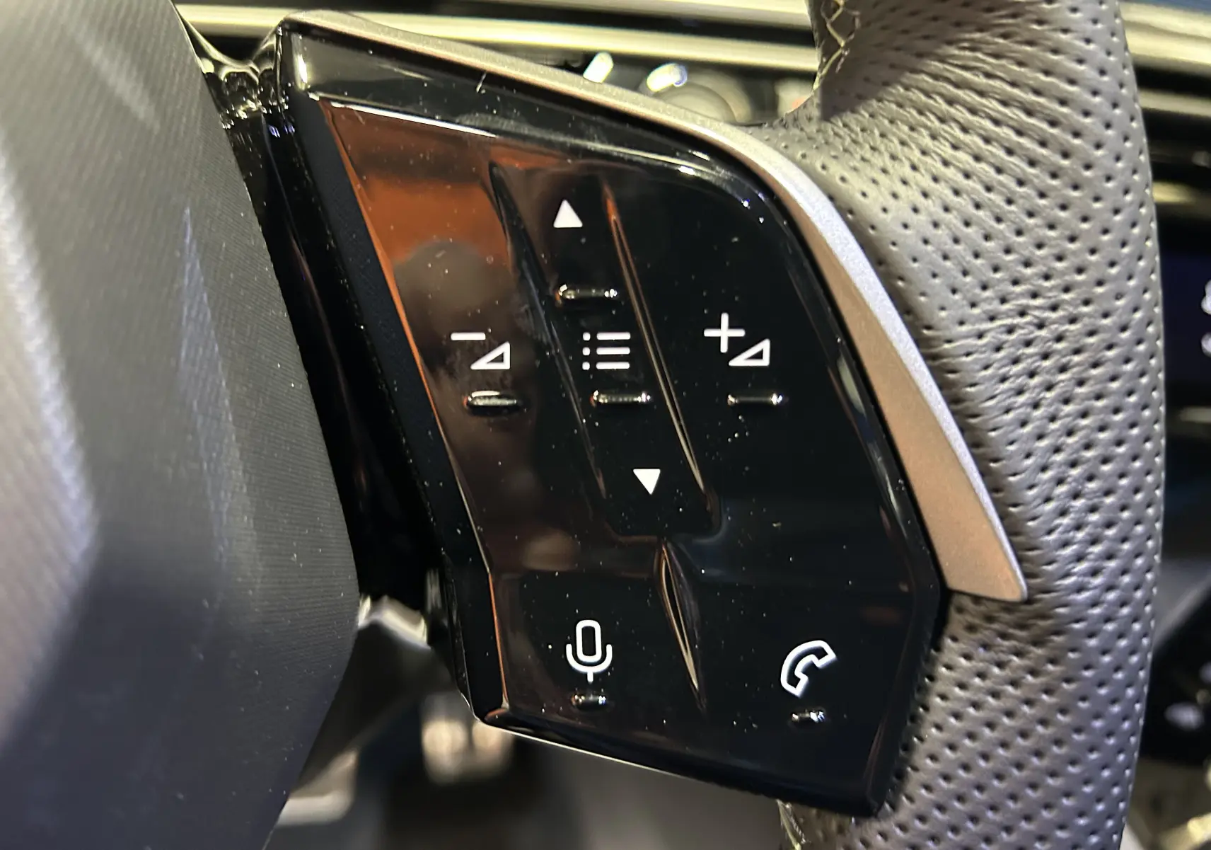 Gros plan sur les commandes noires du volant perforé du Peugeot 5008 III GT Hybrid 145 gris Artense.