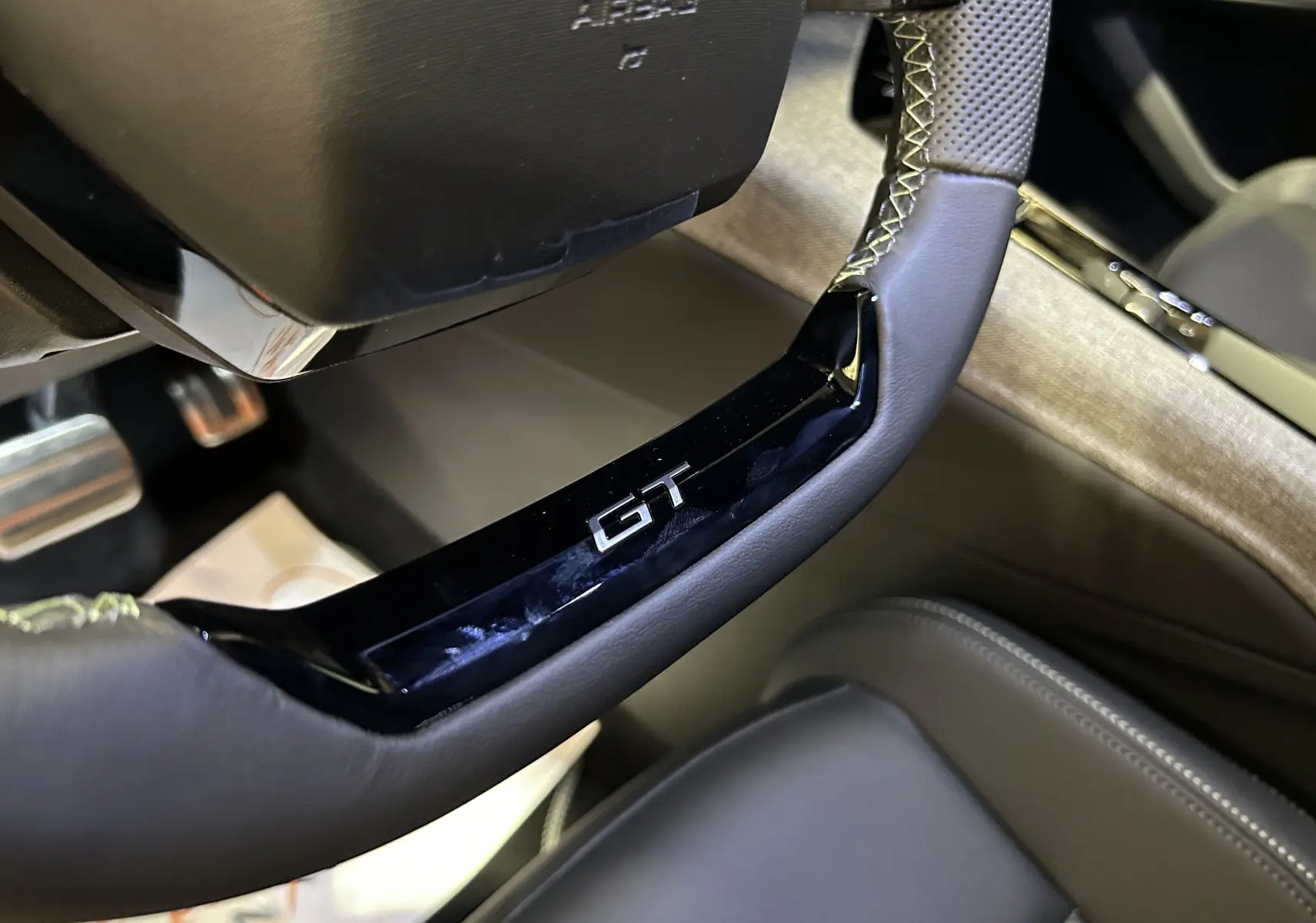 Gros plan sur le volant cuir avec logo GT du Peugeot 5008 III GT Hybrid 145, ambiance intérieure raffinée.