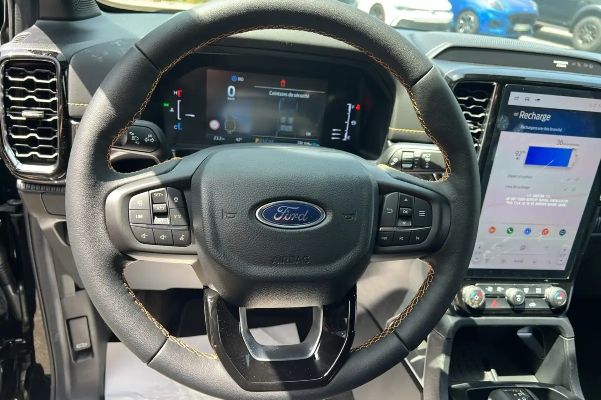 Vue rapprochée du volant noir avec surpiqûres jaunes du Ford Ranger 2025 2.3 PHEV Wildtrak Plus et écran tactile central allumé.