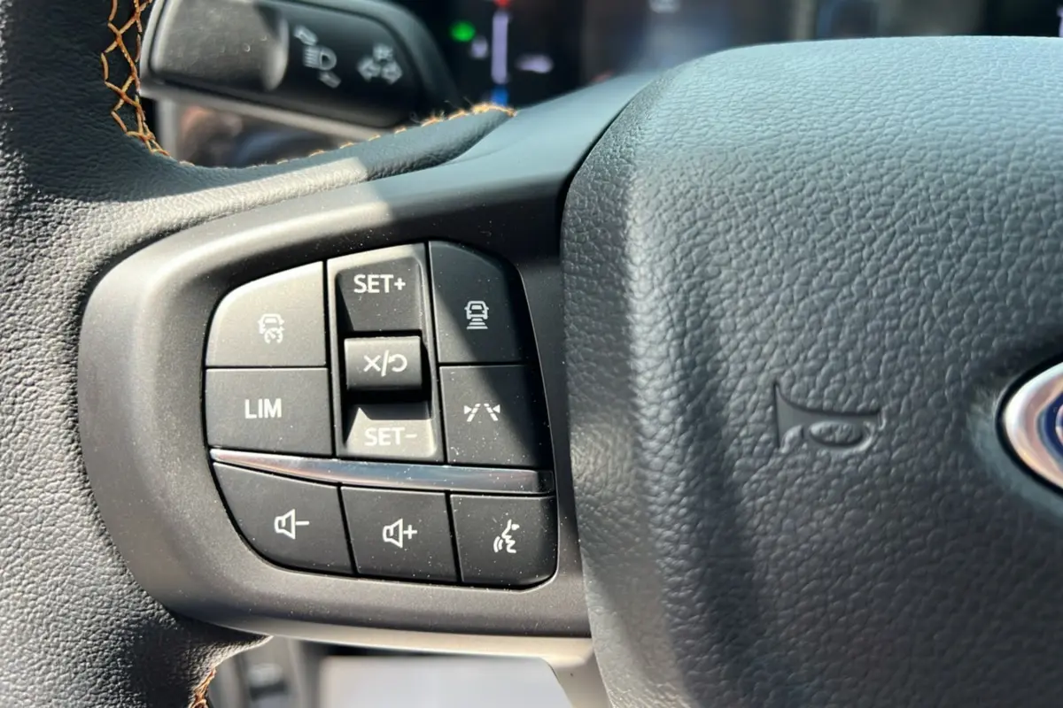 Gros plan sur les commandes à gauche du volant noir du Ford Ranger 2.3 PHEV Wildtrak Plus 2025, avec surpiqûres marron.