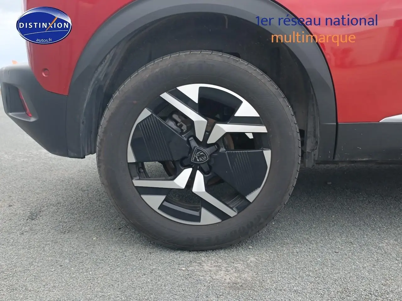 Gros plan sur la roue avant gauche et la jante alu noire et argentée du Peugeot 2008 rouge élixir.