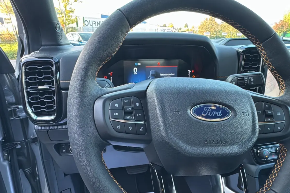 Vue intérieure centrée sur le volant cuir noir avec surpiqûres marron du Ford Ranger PHEV 2025, tableau de bord numérique visible.