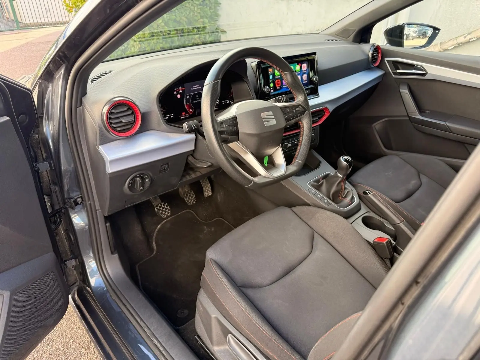 Intérieur côté conducteur de la SEAT Ibiza 2025 gris foncé, volant multifonction et détails rouges autour des aérateurs.