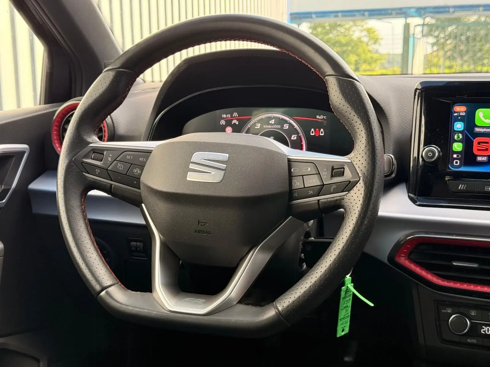 Vue intérieure centrée sur le volant perforé noir avec logo SEAT, tableau de bord numérique et écran tactile à droite.