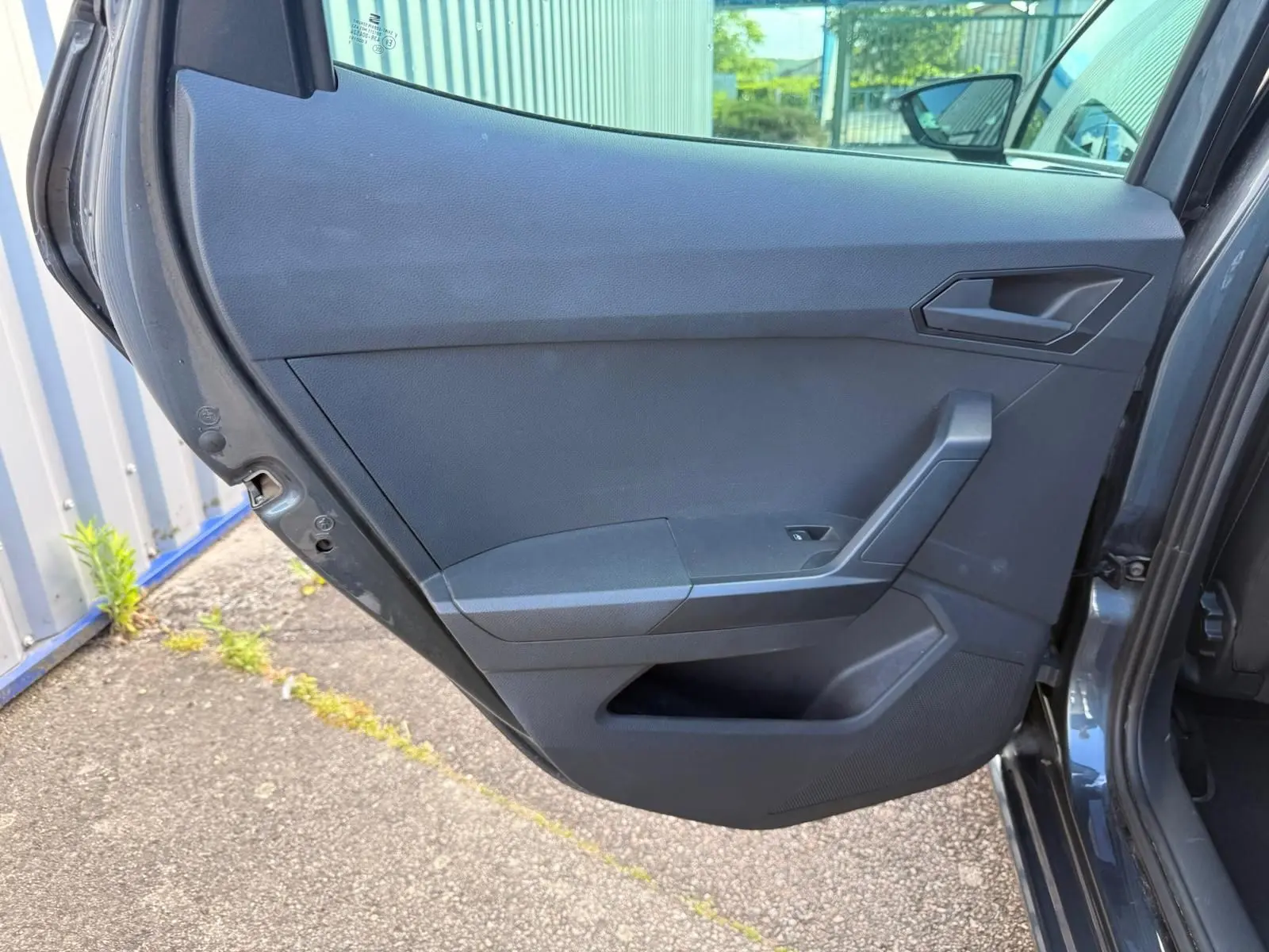 Vue intérieure sur la porte arrière gauche ouverte d'une SEAT Ibiza 2025 gris foncé, avec poignée et commande de vitre.