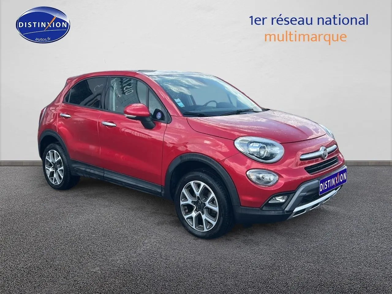 Fiat 500X rouge vue 3/4 avant droit avec jantes alu et barres de toit sur fond neutre.