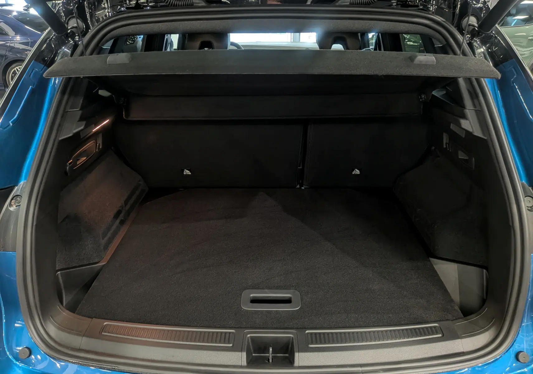 Coffre ouvert vu de l'arrière d'un Renault Austral bleu outremer avec toit noir, intérieur spacieux et tapis noir.