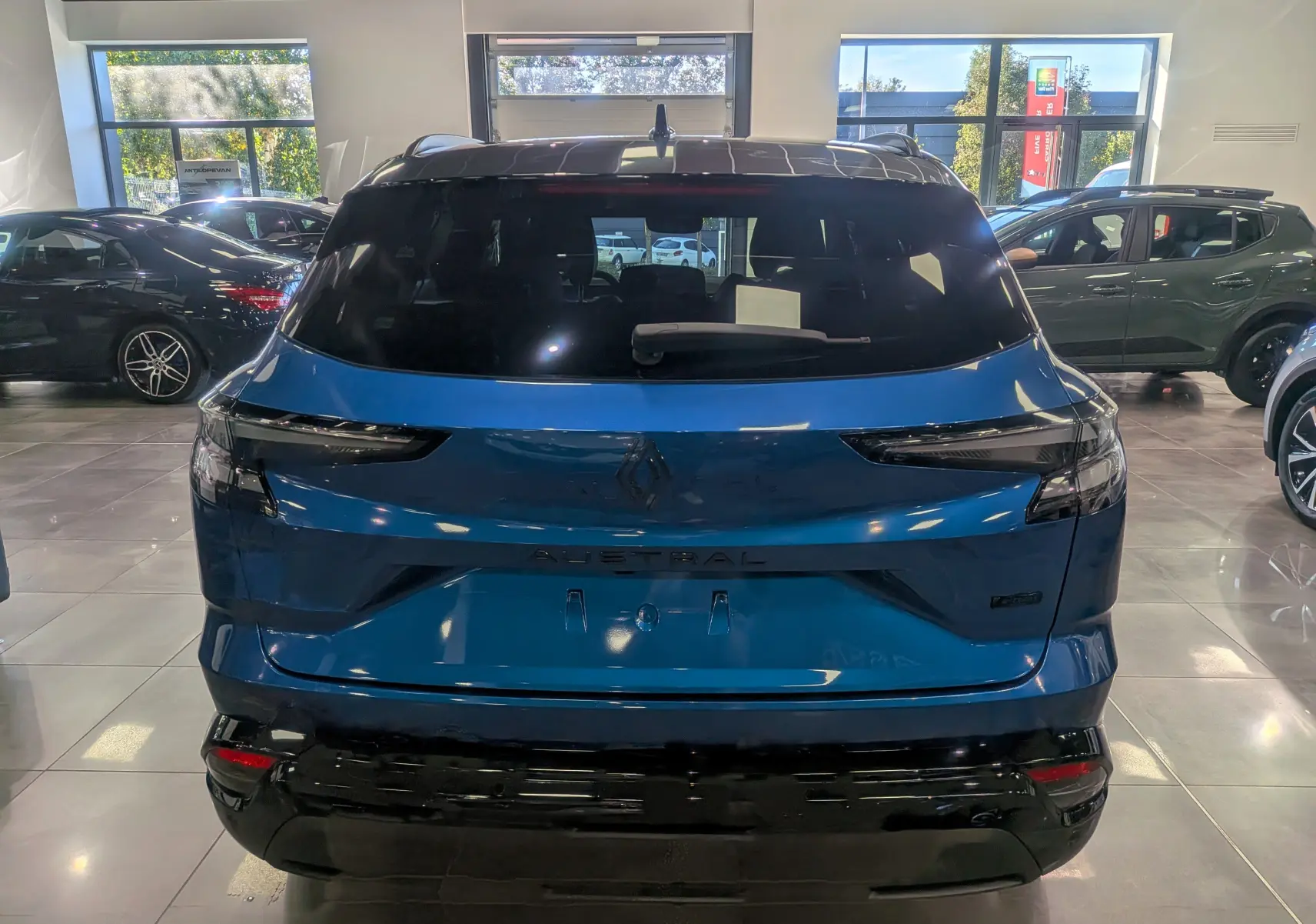 Vue arrière d'un Renault Austral hybride bleu outremer avec toit noir, dans un showroom lumineux.