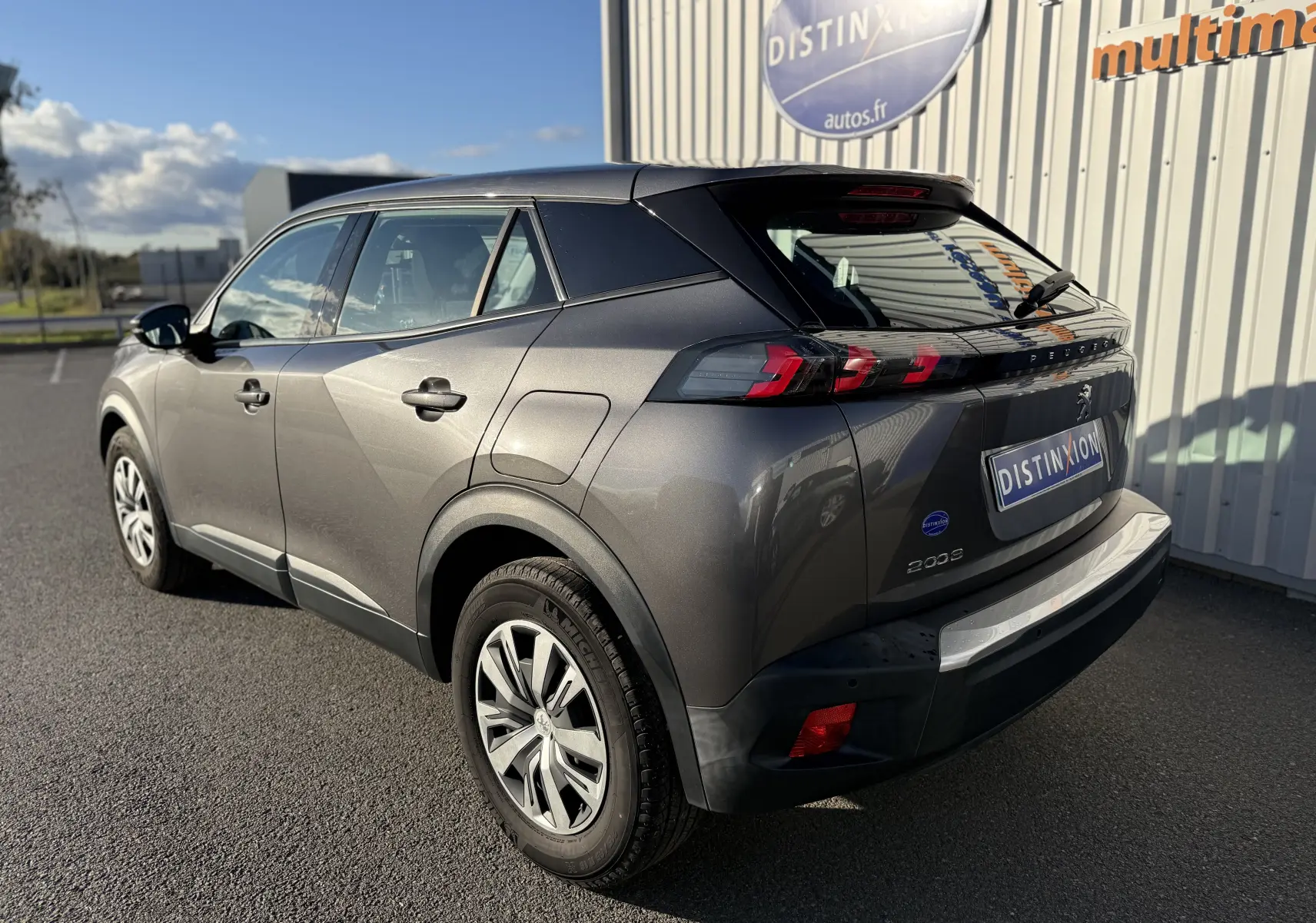 Peugeot 2008 gris vue 3/4 arrière droit, avec feux arrière LED et jantes alliage, stationné devant un bâtiment.