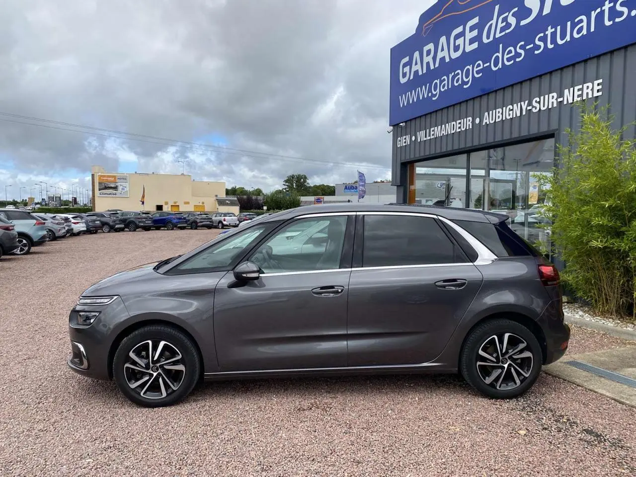 Profil côté gauche d'une Citroën C4 Spacetourer 2019 gris foncé, avec jantes alliage et vitres teintées, stationnée devant un garage.