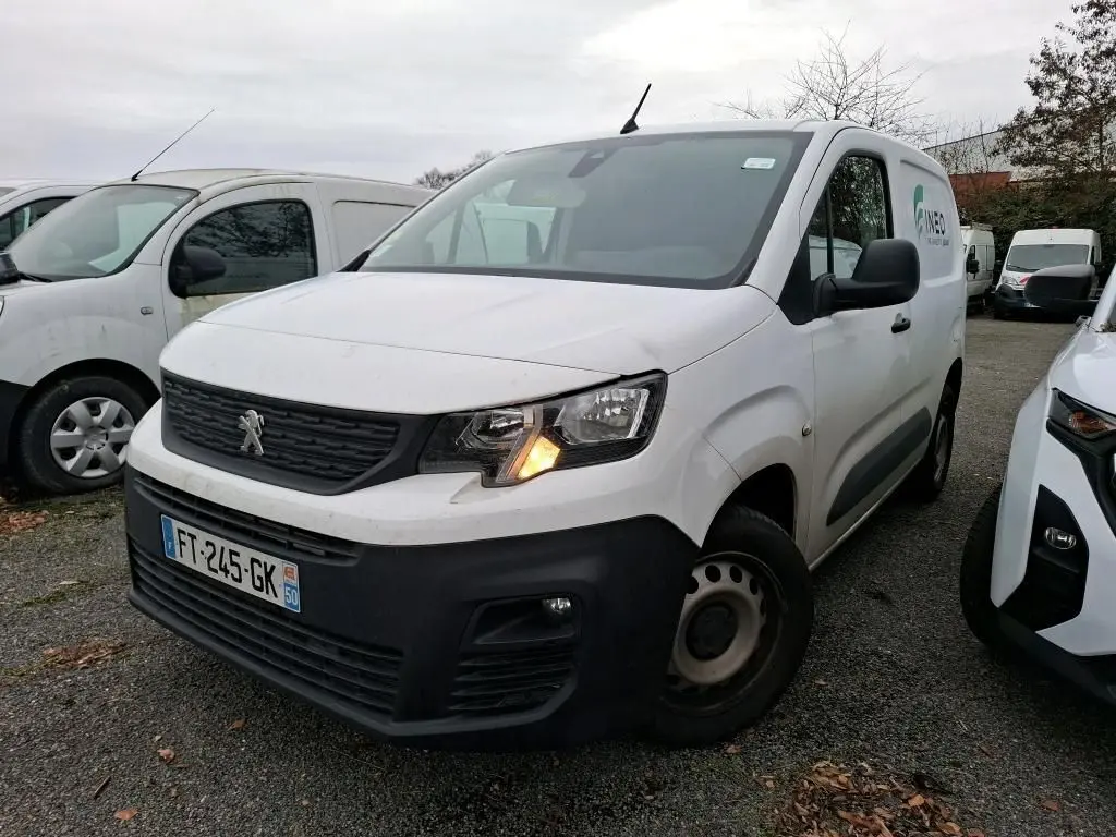 Fourgon Peugeot Partner blanc en 3/4 avant droit avec feu avant allumé sur parking extérieur.