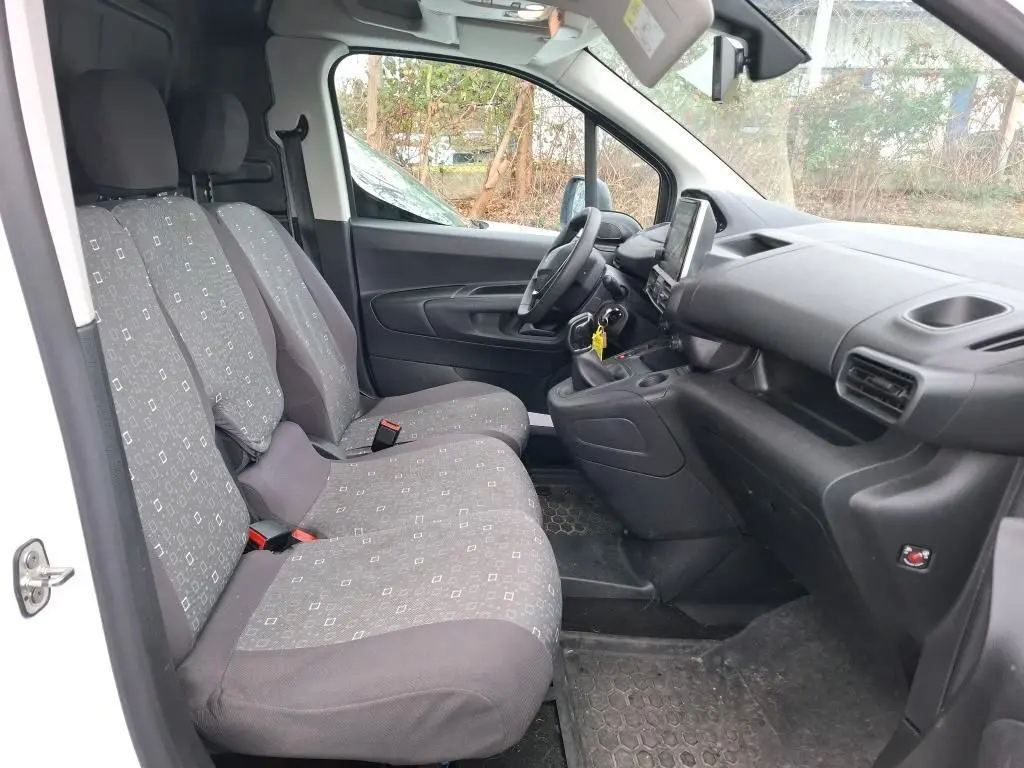 Vue intérieure côté conducteur du Peugeot Partner blanc 2020, montrant les sièges tissu gris et le tableau de bord noir.