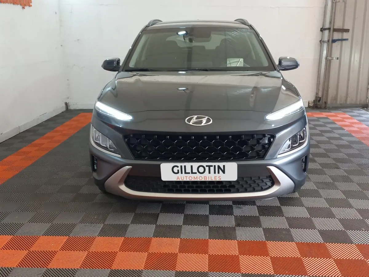 Vue avant d'un Hyundai Kona gris foncé avec feux LED allumés et calandre noire en intérieur showroom.