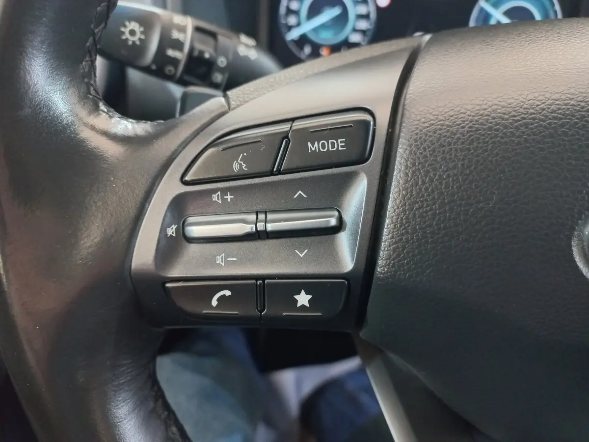 Gros plan sur les commandes gauche du volant en cuir noir du Hyundai Kona 1.6 Hybrid 2022, boutons multifonctions visibles.