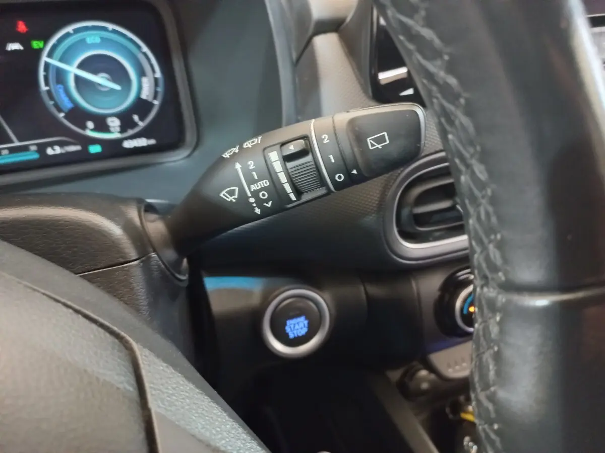 Gros plan sur la commande d’essuie-glace à gauche du volant cuir, avec tableau de bord numérique en arrière-plan.