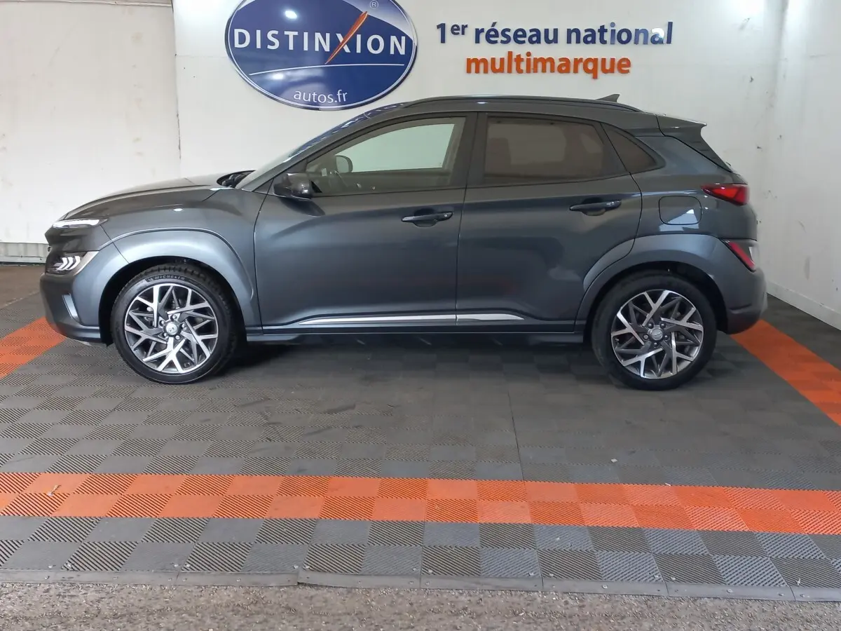 Vue latérale droite d'un Hyundai Kona gris foncé 2022, avec jantes alliage et toit noir contrasté en arrière-plan showroom.