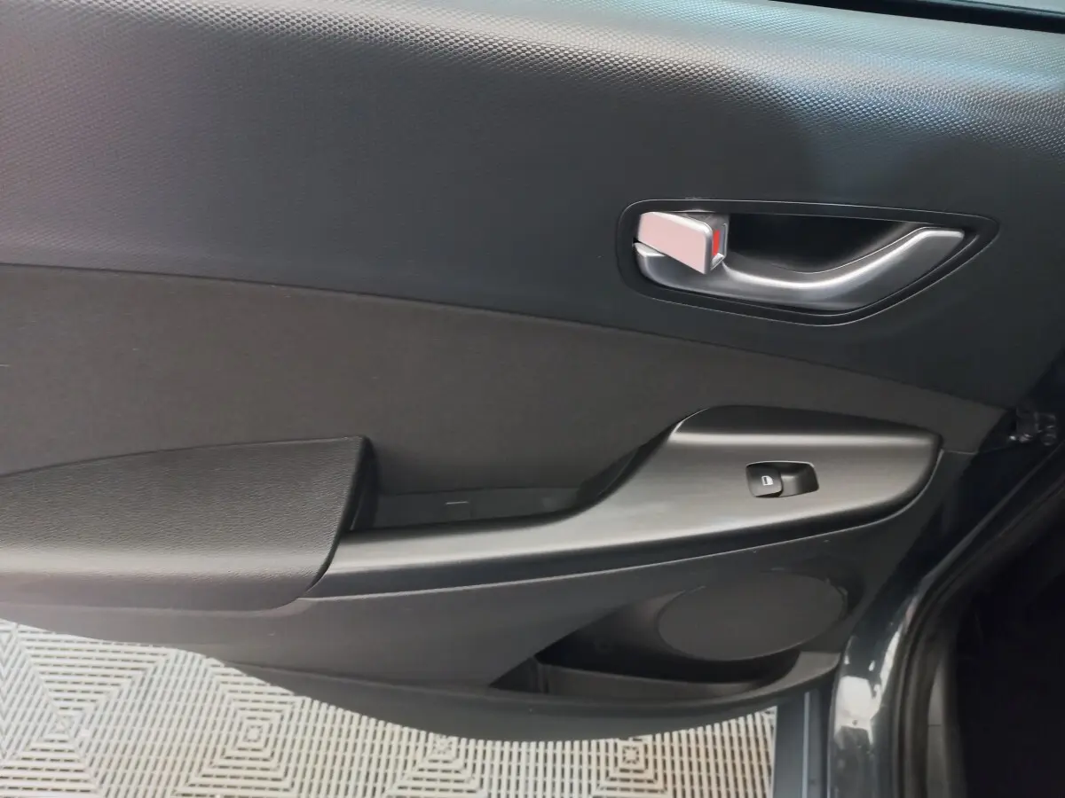 Gros plan sur la porte avant droite grise foncée du Hyundai Kona 2022, avec poignée intérieure argentée et commande de vitre.