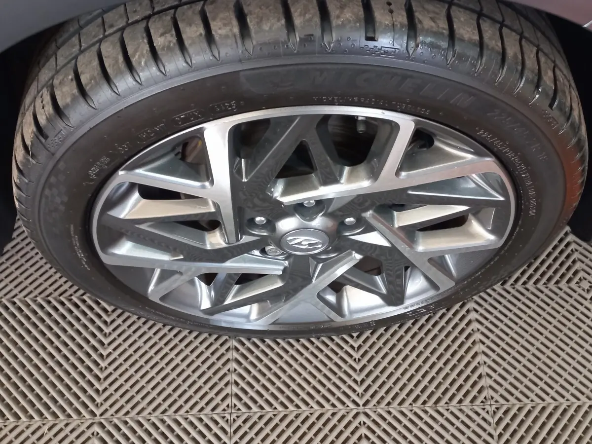 Gros plan sur la roue avant droite avec jante alliage gris et logo Hyundai visible sur un Hyundai Kona gris foncé.