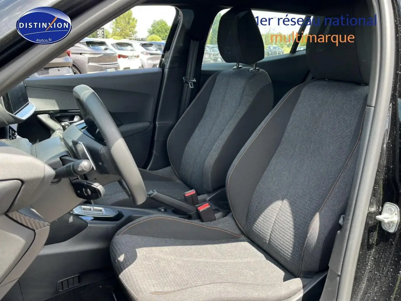 Vue intérieure côté conducteur de la PEUGEOT 2008 noire, montrant les sièges avant en tissu gris et le volant multifonction.