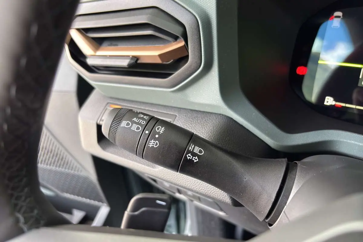 Gros plan sur la commande des feux à gauche du volant du Dacia Bigster Hybrid-G 150 vert cèdre, intérieur moderne.