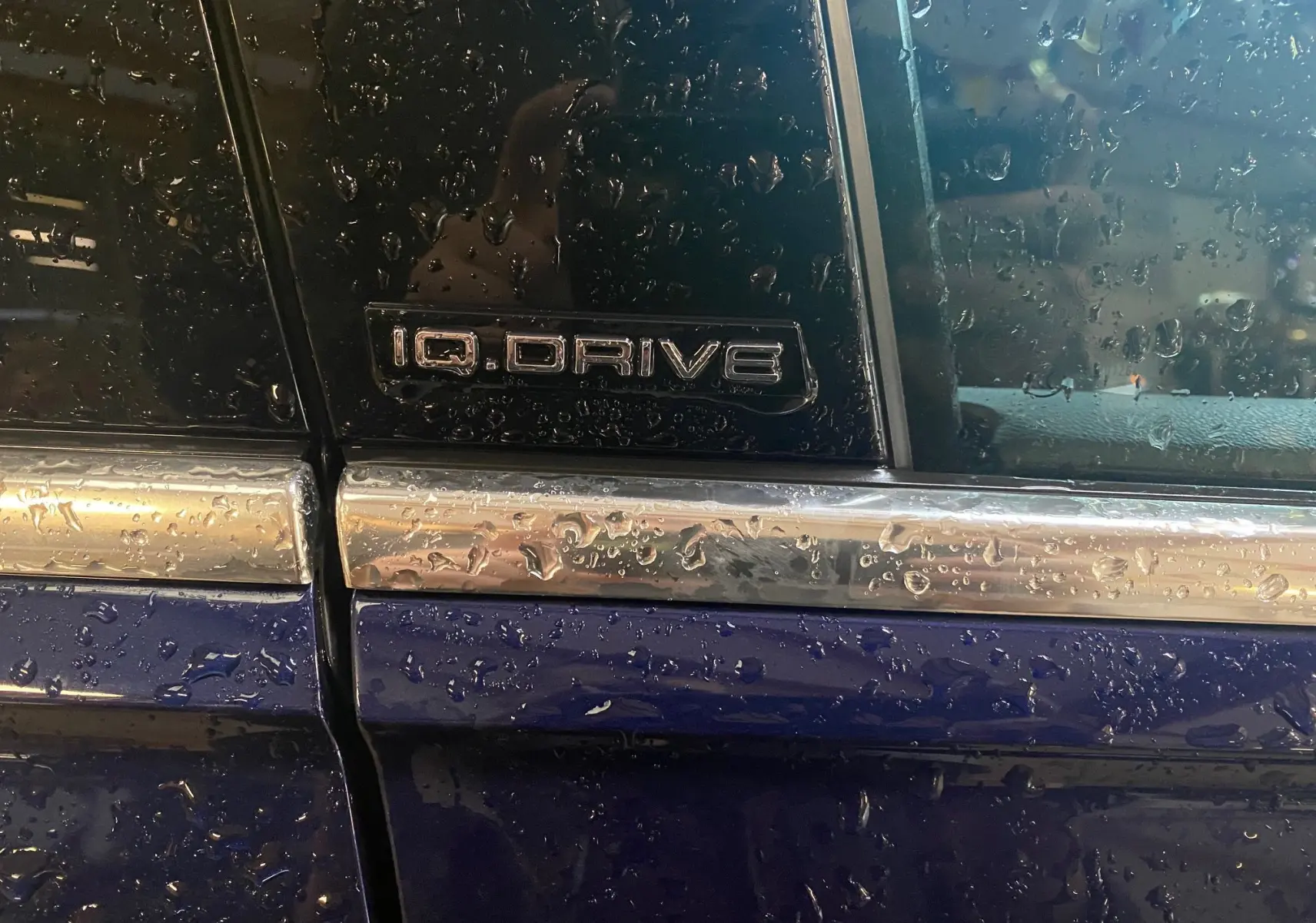 Gros plan sur l’inscription IQ Drive sur la portière côté gauche d’un Volkswagen Tiguan bleu vert mouillé.