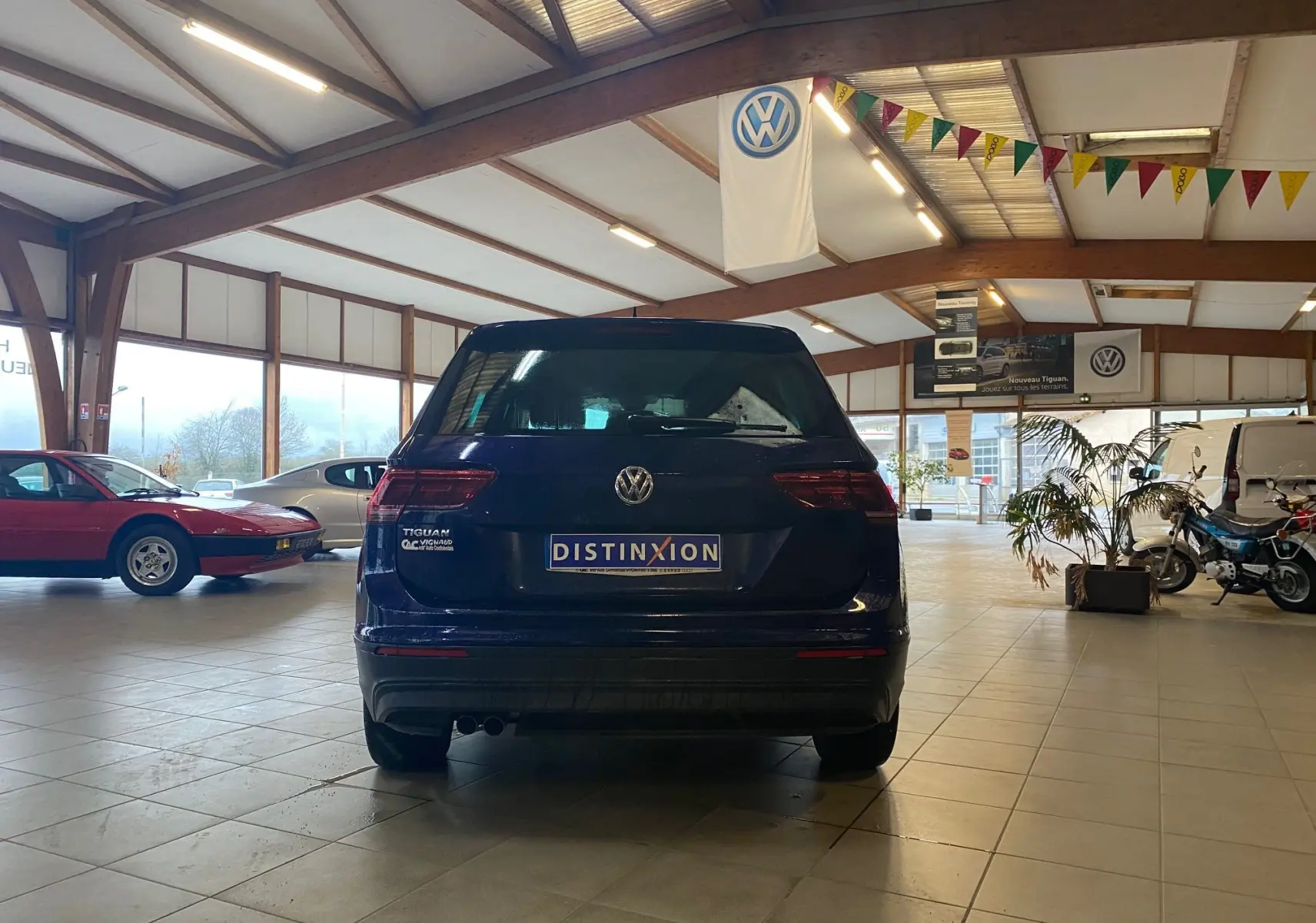 Vue arrière d'un Volkswagen Tiguan bleu vert 2020 dans un showroom avec drapeau VW suspendu au plafond.