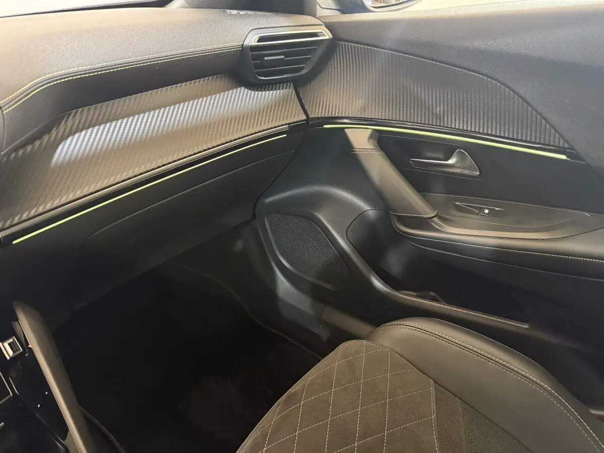 Vue intérieure côté passager du Peugeot 2008 GT Pack 2021, tableau de bord et porte avec surpiqûres et inserts carbone.
