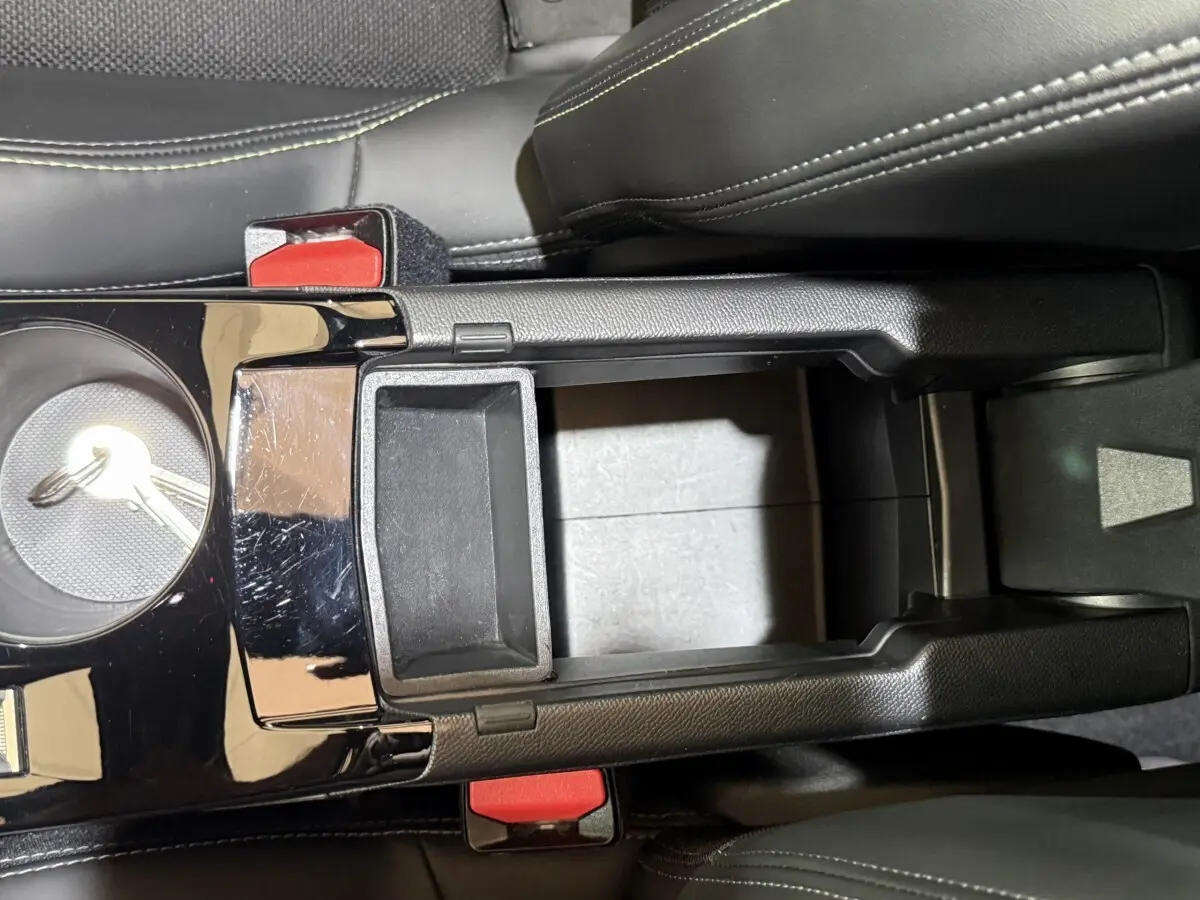 Vue plongeante sur la console centrale noire avec accoudoir ouvert et sièges en cuir noir du Peugeot 2008 bleu.