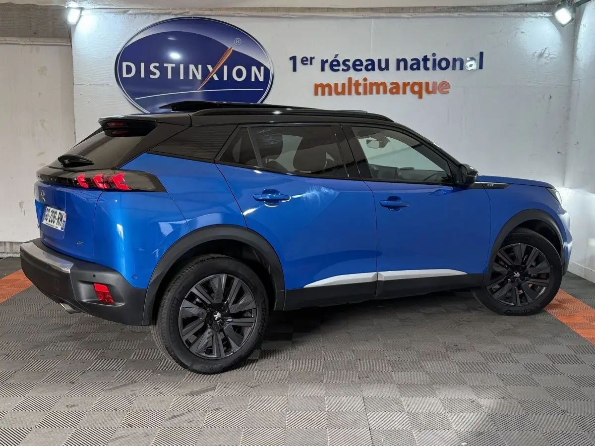Vue côté droit arrière d'un Peugeot 2008 bleu 2021 avec toit noir et jantes noires dans un showroom.