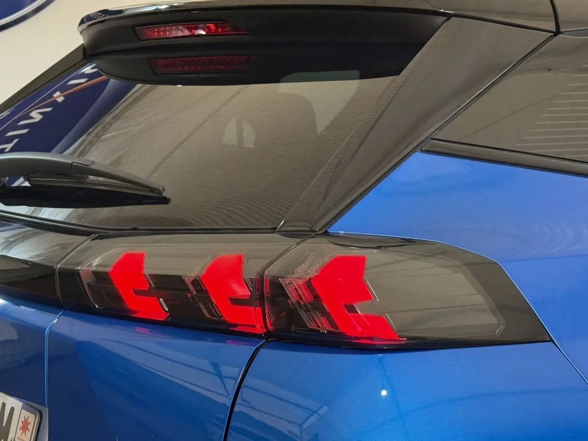 Feu arrière droit allumé sur Peugeot 2008 bleu, vue rapprochée du coin arrière avec lunette et essuie-glace.