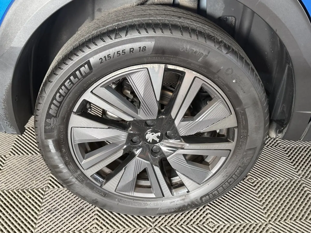 Gros plan sur la roue avant droite du Peugeot 2008 bleu, jante alliage à design moderne avec logo lion au centre.