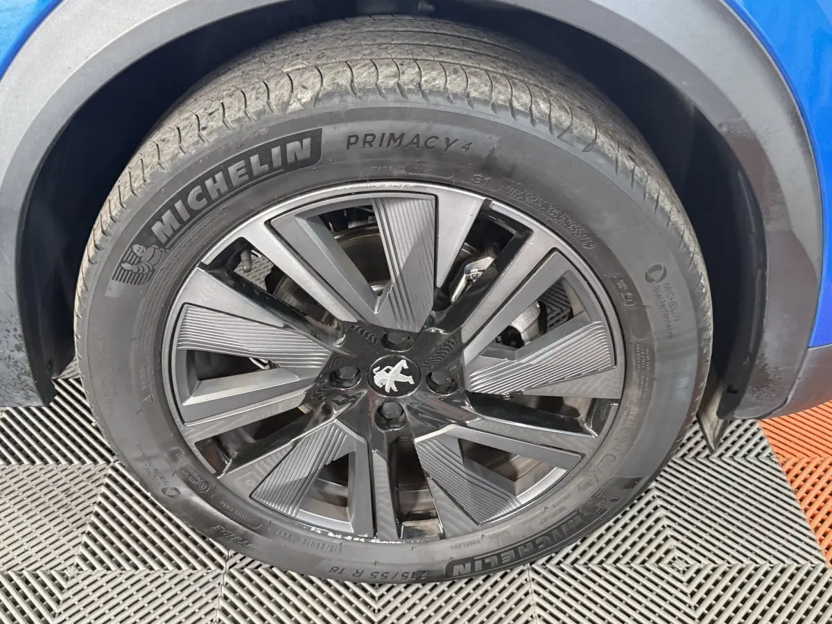 Gros plan sur la roue avant droite d’un Peugeot 2008 bleu, jante alliage noire au design moderne.
